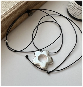 Gros plan détaillé d'un collier avec pendentif fleur en argent sur une surface blanche