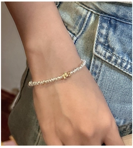 Close-up of minimalist S925 silver and gold two-tone bracelet worn on wrist over denim
