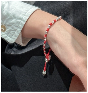 Détail d'un bracelet en corde tressée rouge avec perles en argent sur un poignet