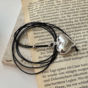 Minimalist silver heart pendant necklace with black cord on a vintage background