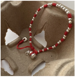 Détail macro du bracelet en corde rouge tressée avec perles et pendentif argentés
