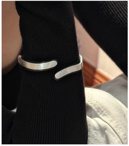 Detail of silver wavy texture bracelet worn over black ribbed knit sleeve cuff