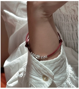 Close-up of a red woven rope bracelet with silver beads and a central ingot-shaped charm
