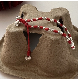 Détail d'un bracelet en corde tressée rouge avec des perles en argent polies