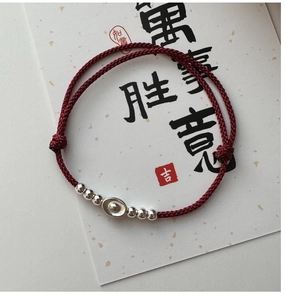 Macro detail of S925 sterling silver sycee charm on a red braided bracelet string