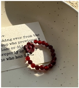 Detail of S925 silver red agate beaded ring with delicate floral charm on ceramic dish