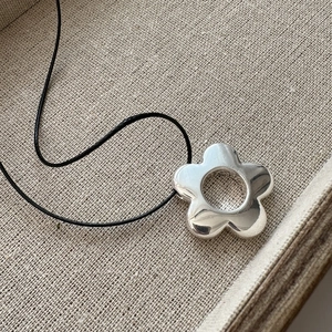 Pendentif fleur ajourée en argent 925 avec cordon noir sur fond texturé beige