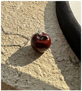 Macro shot of minimalist red enamel apple pendant with silver leaf on a textured stone base