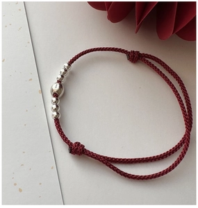 Macro shot of red braided bracelet with adjustable slip knot and silver bead details