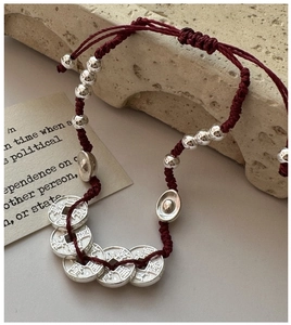 Détail d'un bracelet en corde rouge tressée avec pièces en argent S925 et breloque
