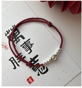 Close-up of red woven bracelet with silver beads and ingot charm on a decorative card