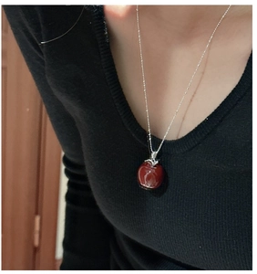 Detailed close-up of a red apple pendant necklace with silver ball chain on a model