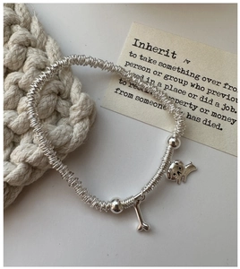 Detail of silver S925 beaded bracelet with cute puppy and bone charms on woven texture