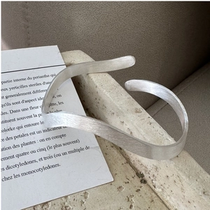 Close-up of wavy brushed silver cuff bracelet on stone pedestal with minimalist aesthetic