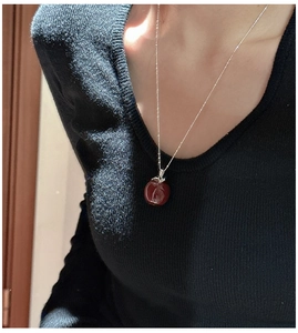 Detail of a minimalist S925 silver necklace featuring a glossy red apple pendant on a model