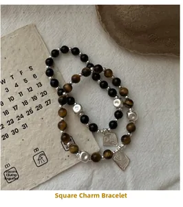 Dettaglio di bracciali con perline di occhio di tigre e ciondoli quadrati in argento