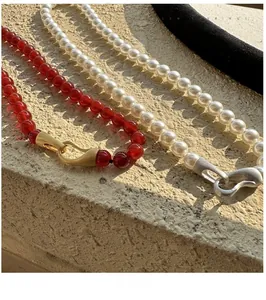 Macro detail of beaded necklaces with red stones and pearls featuring matte metal clasps