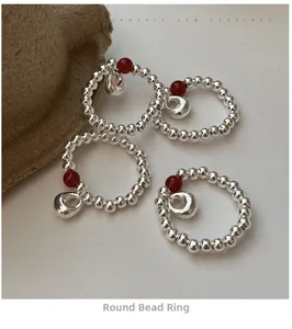 Detail of silver beaded rings with red agate stones and small pendants on a neutral base