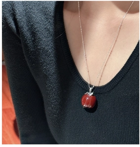 Macro shot of silver apple necklace with red resin pendant on black sweater
