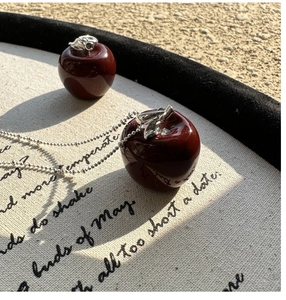 Close-up of red apple pendant with silver leaf detail on vintage poetic fabric