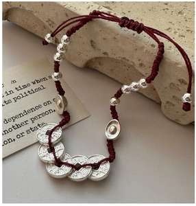 Détail du bracelet en corde rouge tressée avec pièces en argent S925 et breloques