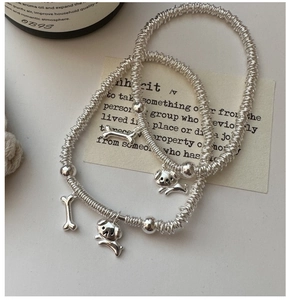 Detailed shot of elastic silver puppy and bone charm bracelets on an aesthetic background