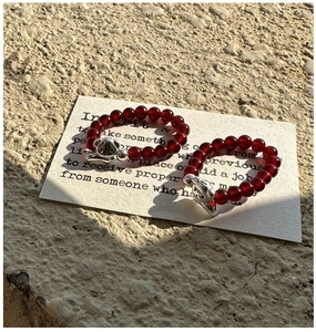 Détail de deux bagues en perles rouges ornées de breloques en forme de petit chien argenté