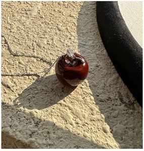 Close-up of red apple pendant with silver chain on textured outdoor surface
