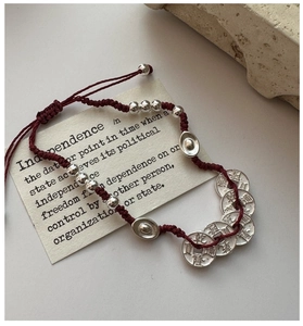 Détail d'un bracelet tressé rouge avec lingots d'argent et pièces sur pierre
