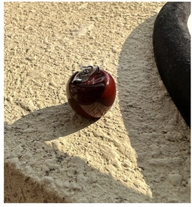 Detail of red apple pendant with silver leaf on textured stone background