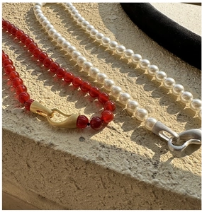 Detail of red agate and pearl necklaces with matte metallic S-buckles on stone
