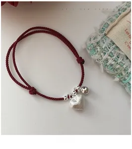 Macro detail of red woven cord bracelet with matte heart pendant and silver beads