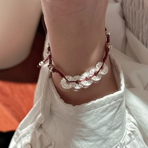 Bracelet en cordon rouge fait main avec pièces en argent S925 au poignet d'une personne