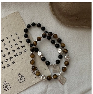 Dettaglio dei bracciali con occhio di tigre e perline nere e ciondoli incisi