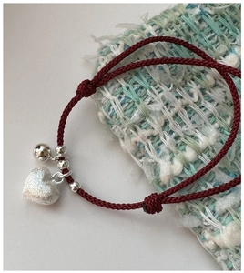Detailed macro of a red woven cord bracelet with S925 silver heart and bell charms