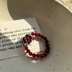 S925 silver red agate beaded ring with flower charm and metallic accents on ceramic plate