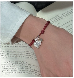 Detail of red braided cord bracelet with brushed silver heart and bell charm on wrist