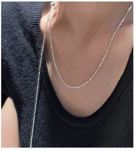 Macro detail of minimalist S925 silver beaded necklace on black knitwear
