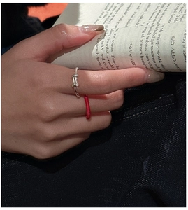 Detail of silver T-shaped ring with red string on finger while holding a book
