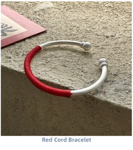 Détail d'un bracelet jonc argenté avec cordon rouge tressé et embouts sphériques