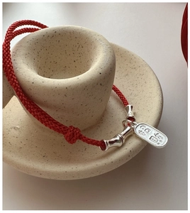 Macro detail of red woven cord bracelet with bamboo silver tube and lucky charm