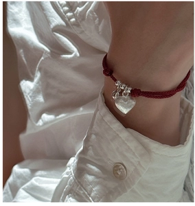 Detailed close-up of a red woven rope bracelet with silver beads and heart charm on wrist