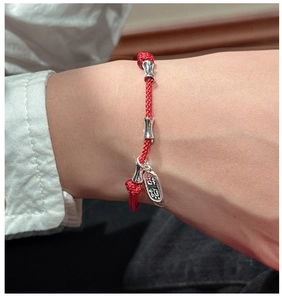 Detail of red braided lucky bracelet with silver bamboo beads and auspicious charm