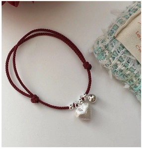 Macro detail of red woven rope bracelet with brushed heart charm and small silver bell