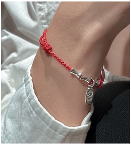 Detail of red braided cord bracelet with silver bamboo-shaped charms on wrist