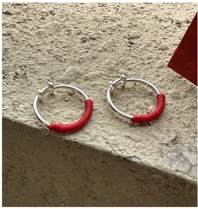 Macro shot of silver horseshoe buckle earrings wrapped in festive red silk cord