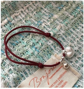 Detail of red woven rope bracelet with matte heart pendant and silver bell on fabric