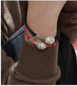 Detail of red and black woven bracelets with silver tortoise pendants on sweater sleeve