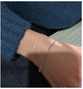 Detail of layered S925 silver bracelets with white zircon and black bead accents on wrist