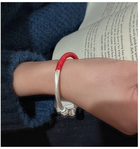 Détail d'un bracelet jonc en argent mat avec fil rouge sur fond de manche en tricot